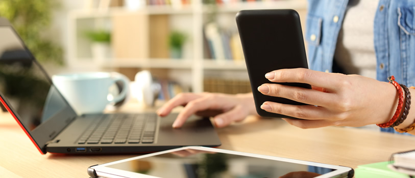 A laptop and tablet on a table. Person in the background holding a phone.