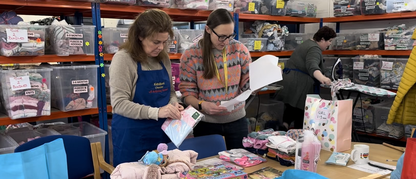 Two people sorting through donations to the KidsBank Chester whilst another irons donated clothes in the background.