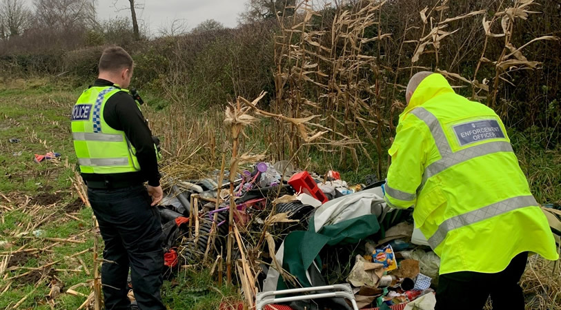 A Police Officer and Council Enforcement Officer going through fly-tipped rubbish in a field as part of Operation Flycatcher.