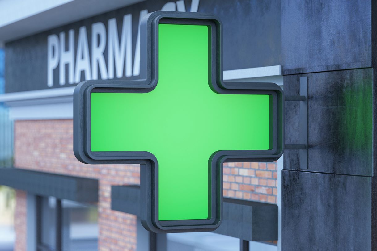 Green cross sign suspended on the side of a building displaying the word Pharmacy